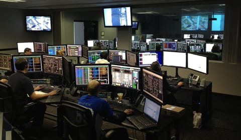 Operations room with operators at multi-monitor desks and wall displays