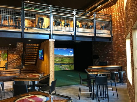 Golf simulator bay inside a lounge with seating and a bar area